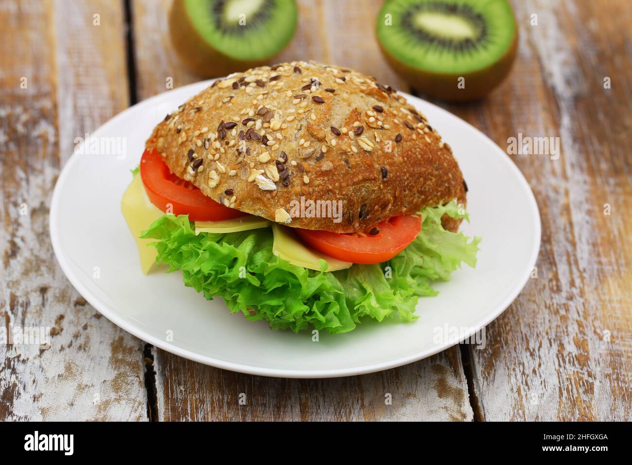 Whole grain roll with cheese, lettuce and tomato on white plate on rustic wood Stock Photo