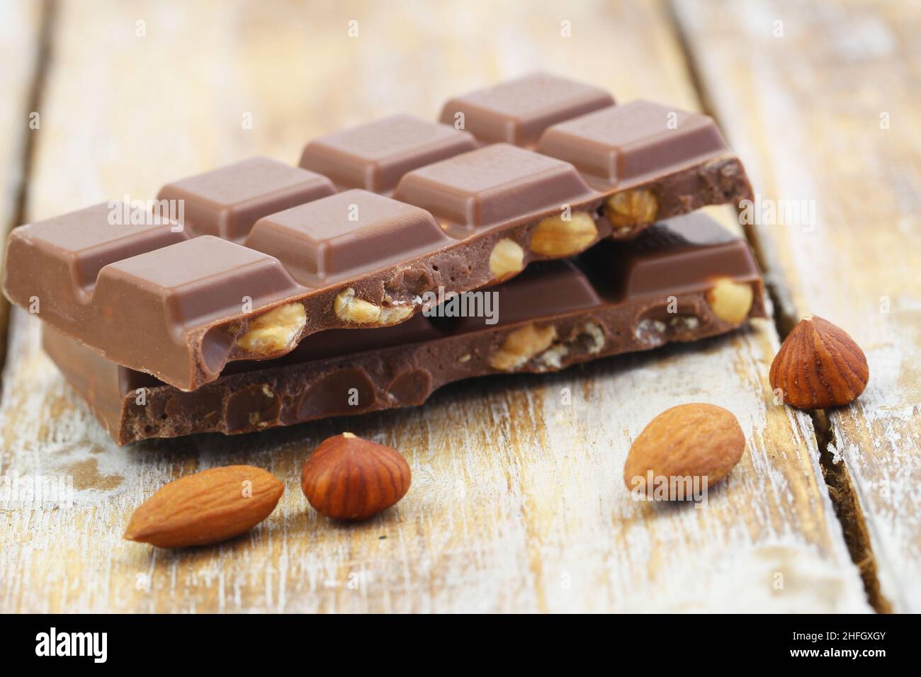 Two milk chocolate pieces with whole hazelnuts and almonds on rustic wooden surface Stock Photo