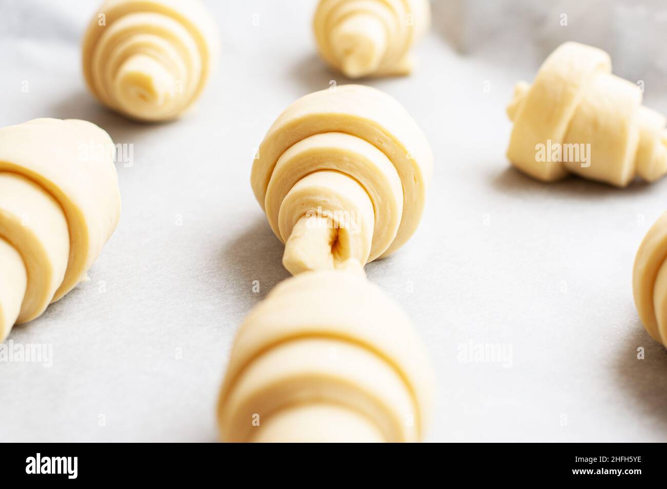 Semifinished or unbaked croissant on a baking sheet. Puff pastry baking. Close up. Stock Photo