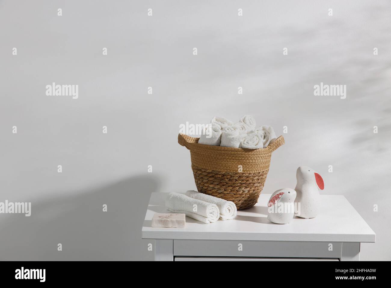 A wicker basket with rolled face towels, soap, two ceramic figurines of