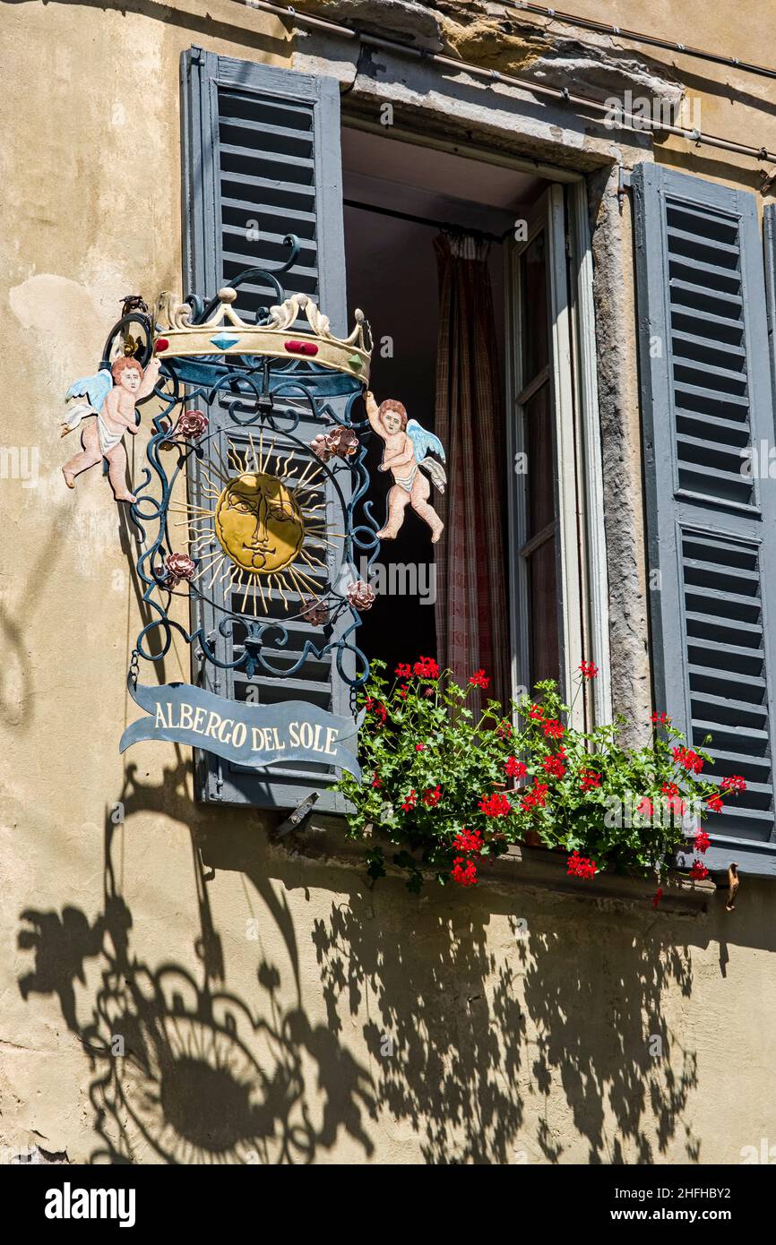 The artful guild sign of the hotel Albergo del Sole, next to an open window with shutters. Stock Photo