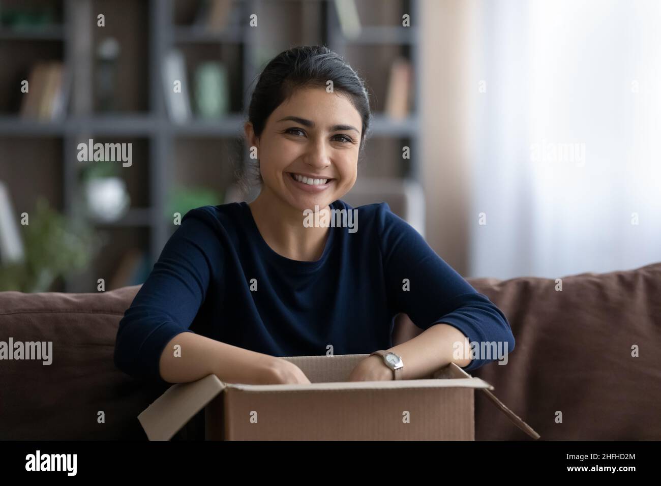 Portrait of happy young Indian woman unpacking carton box. Stock Photo