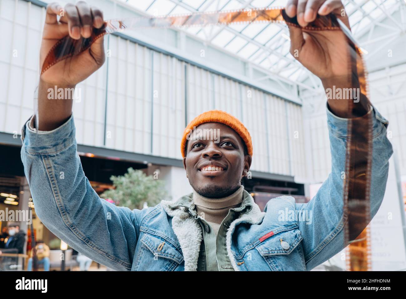 Emotional happy African-American man photographer in denim jacket looks at vintage film in brightly lit room extreme closeup Stock Photo