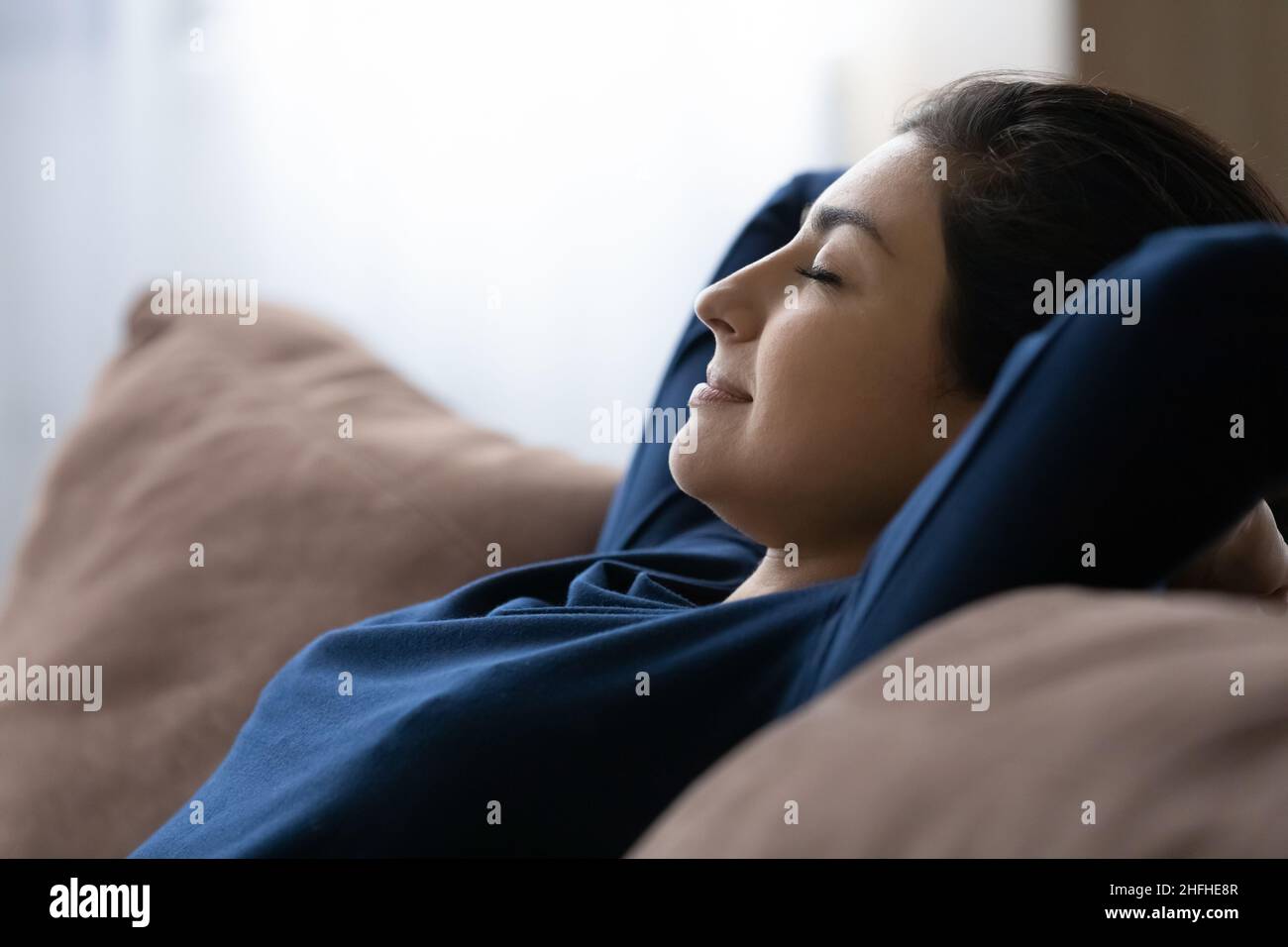 Peaceful happy young Indian woman resting on cozy sofa. Stock Photo