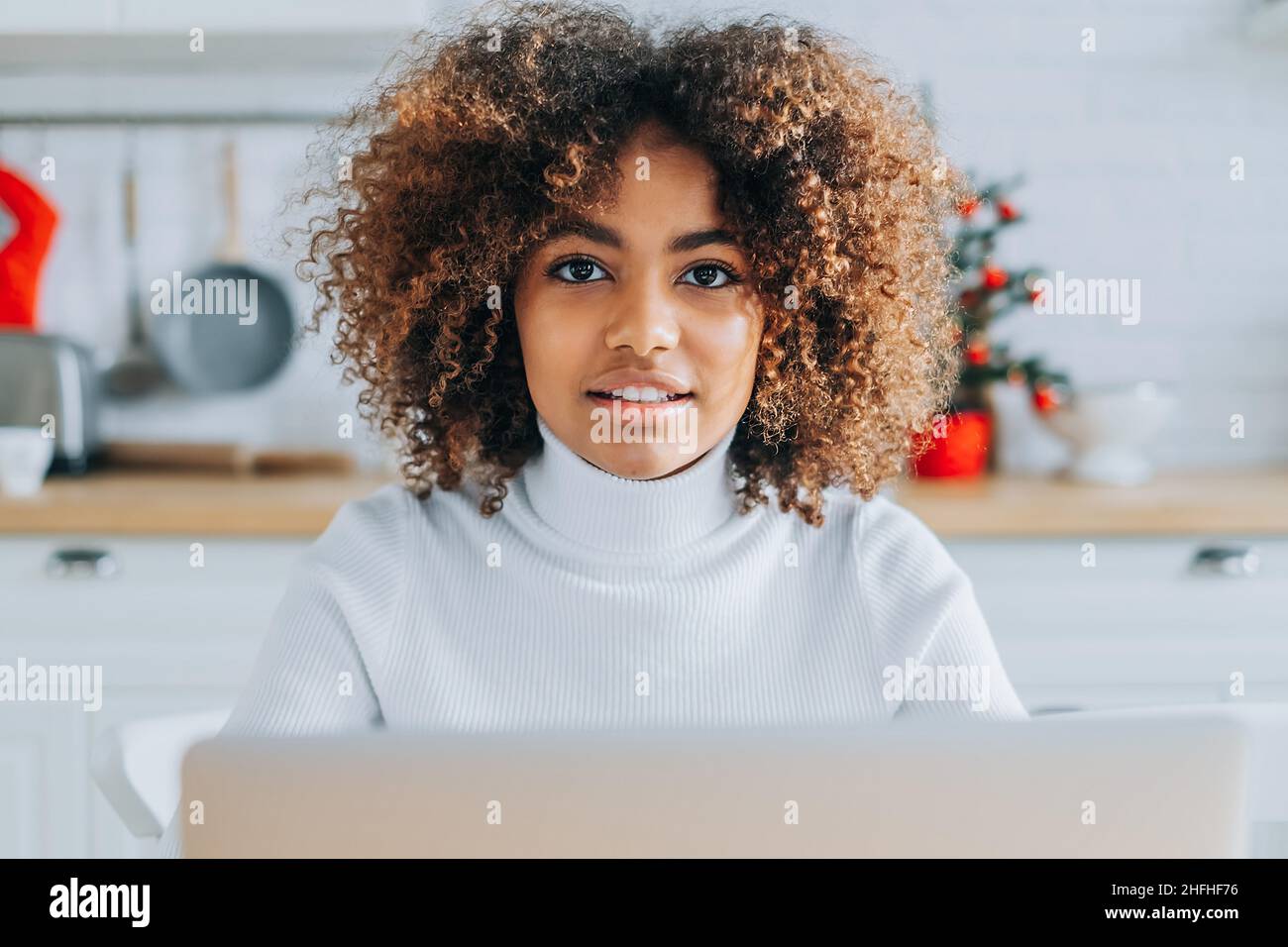 Concentrated and excited dark skinned young buyer with trendy hair looks in laptop smiles and enjoys online shopping closeup Stock Photo
