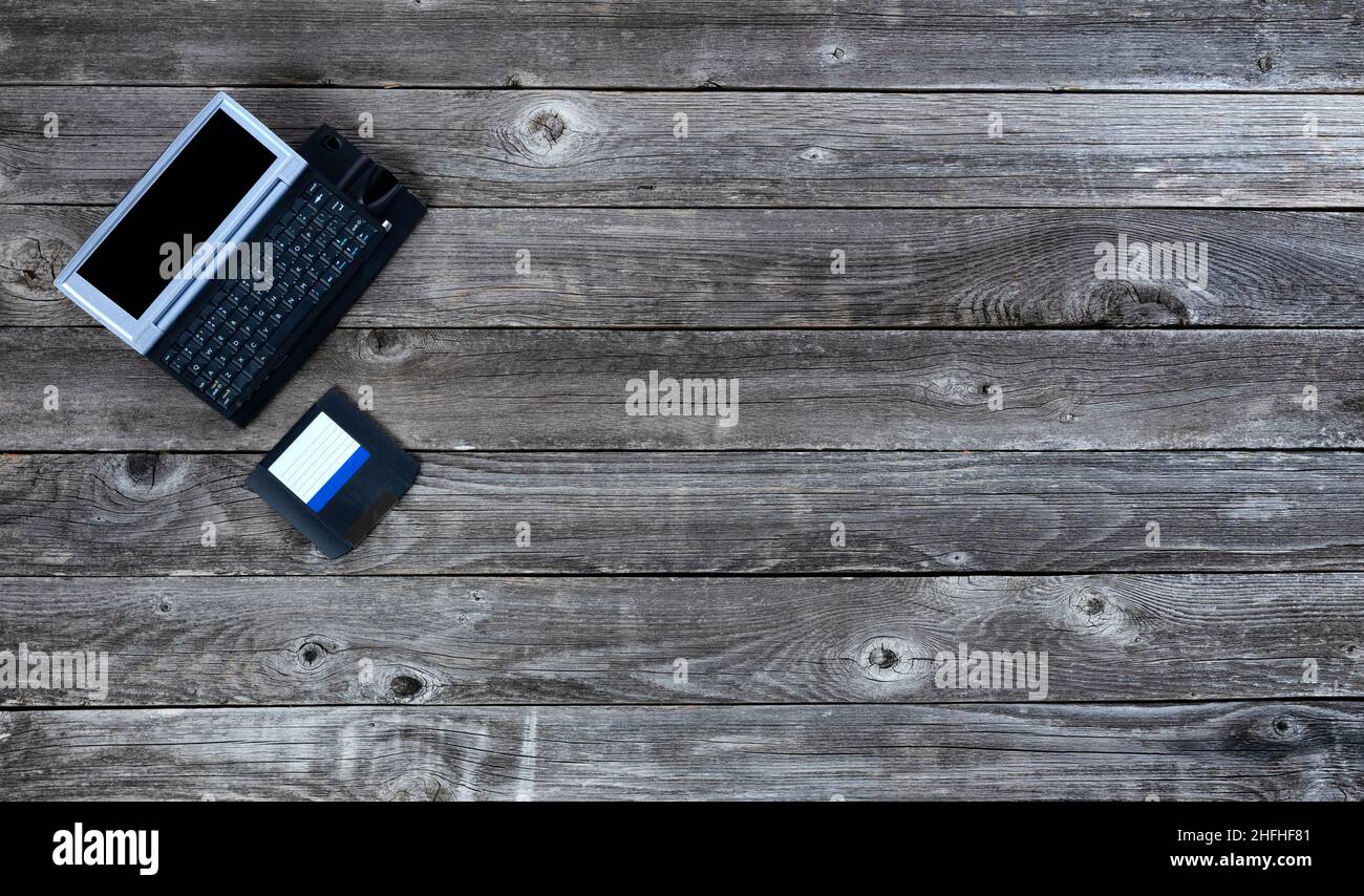 Aged wood office desk table with retro technology of a portable computer and floppy data disk. Top view with plenty of copy space. Stock Photo