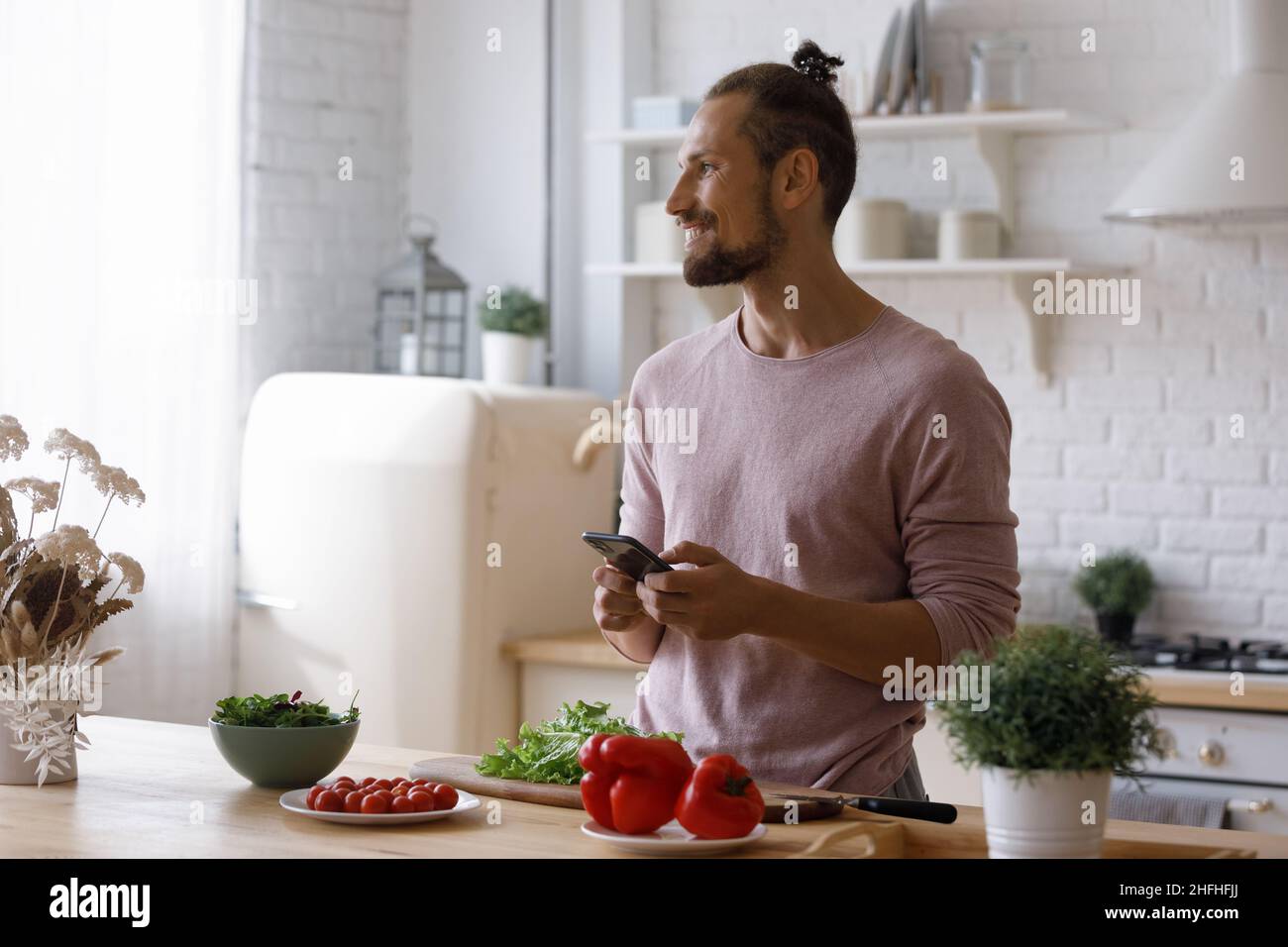 Happy young man using cellphone, preparing food. Stock Photo