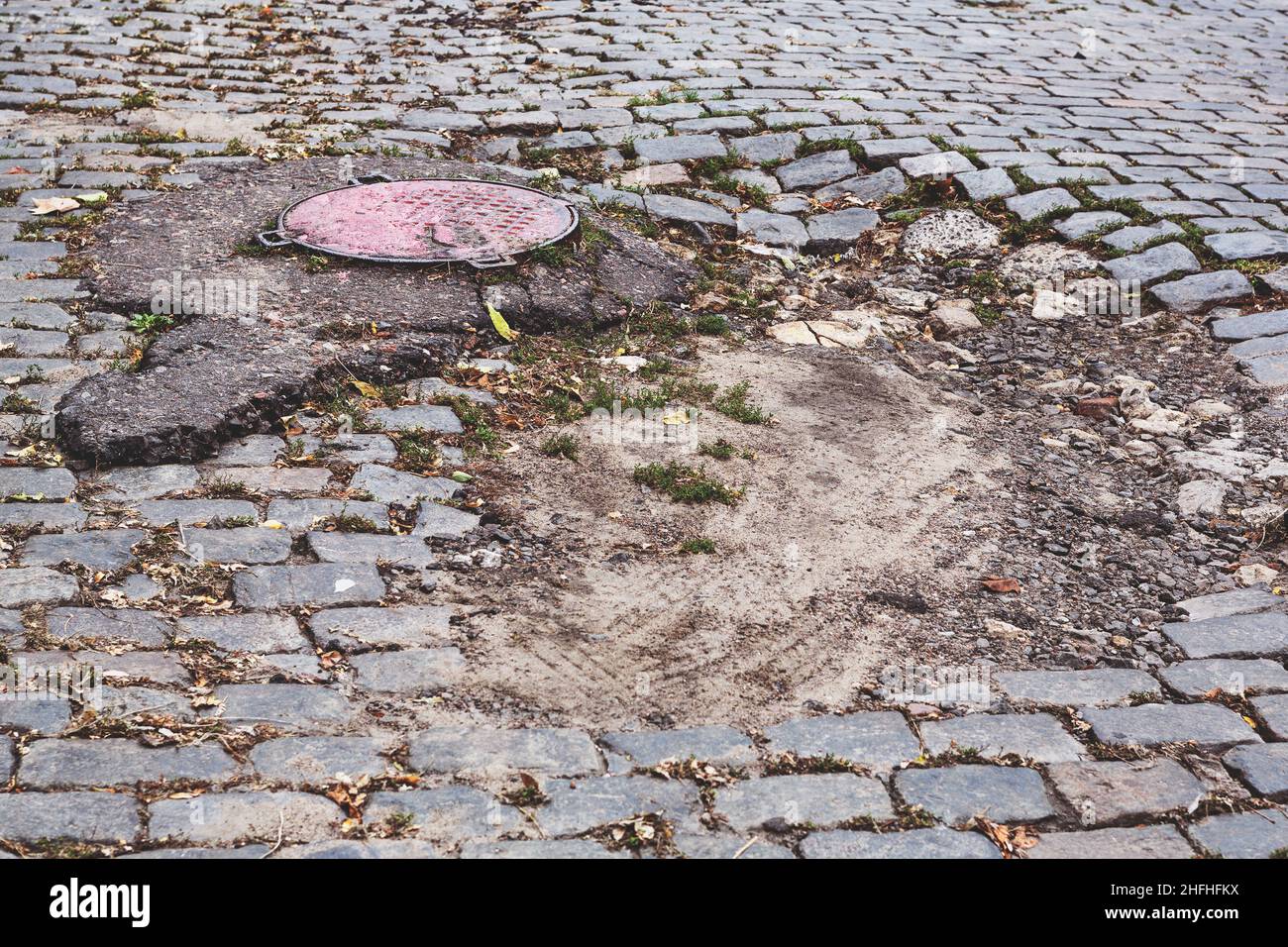A road damaged by rain and snow, that is in need of maintenance. Broken asphalt pavement resulting in a pothole, dangerous to vehicles. Stock Photo