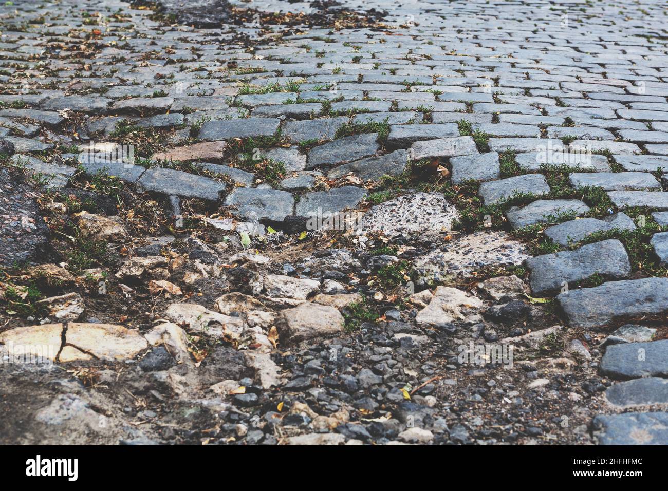 A road damaged by rain and snow, that is in need of maintenance. Broken asphalt pavement resulting in a pothole, dangerous to vehicles. Stock Photo