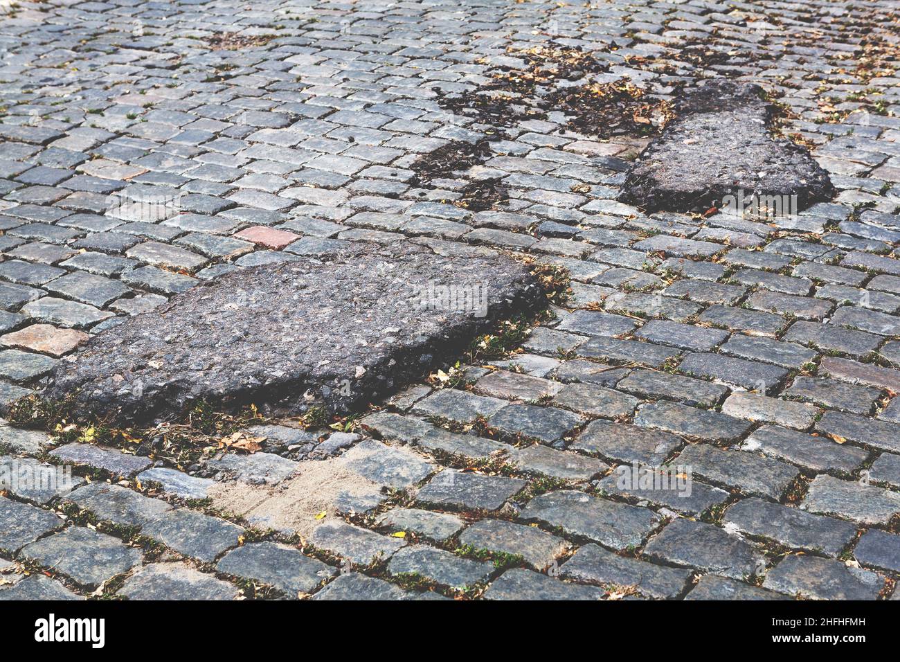 A road damaged by rain and snow, that is in need of maintenance. Broken asphalt pavement resulting in a pothole, dangerous to vehicles. Stock Photo