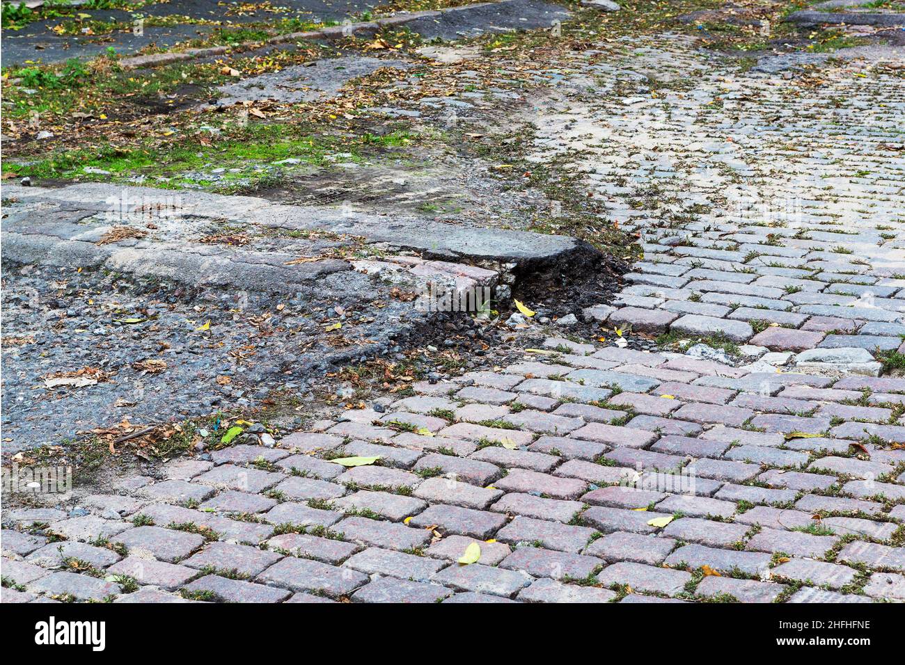A road damaged by rain and snow, that is in need of maintenance. Broken asphalt pavement resulting in a pothole, dangerous to vehicles. Stock Photo