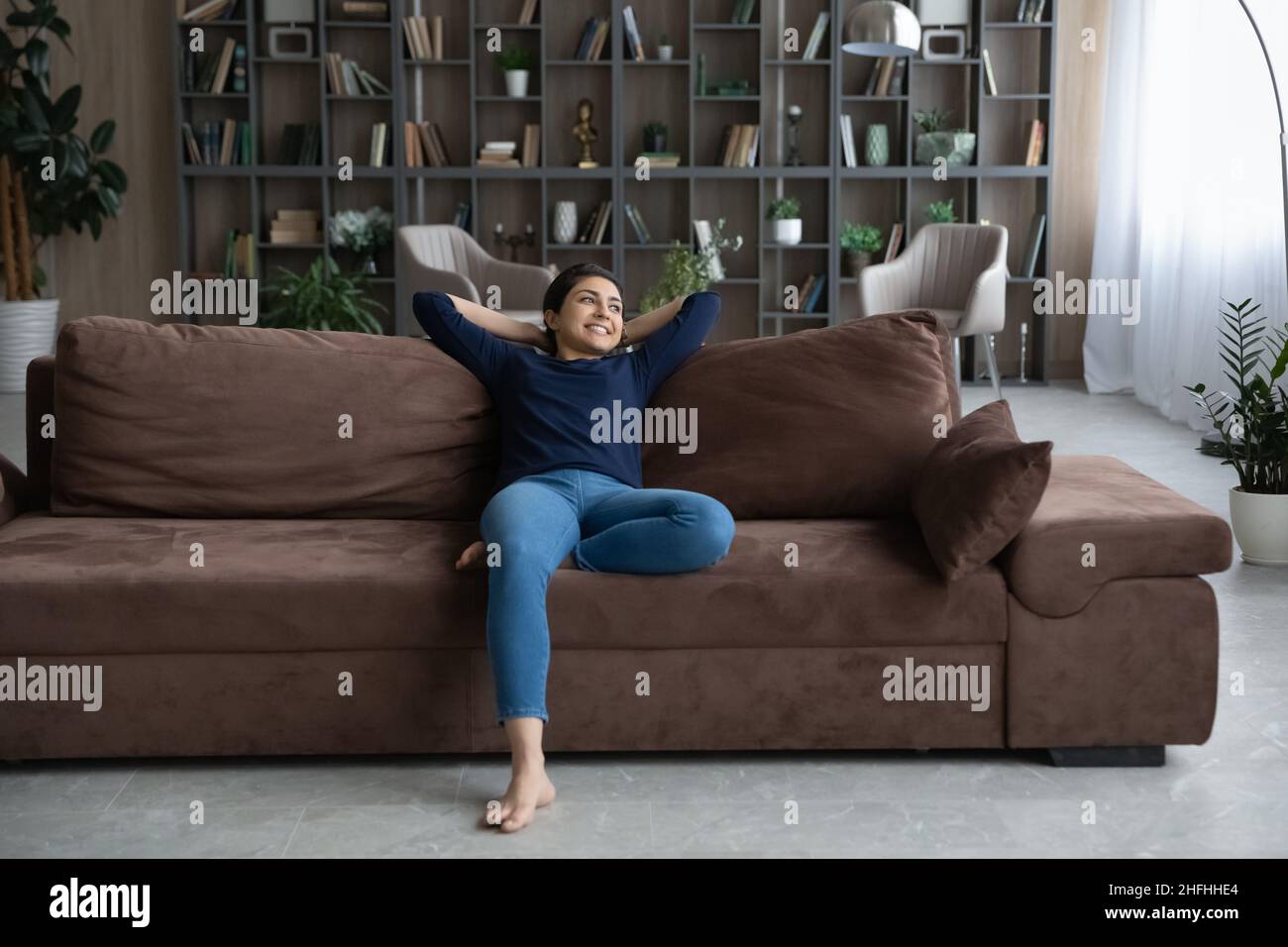 Happy young female Indian homeowner resting on sofa. Stock Photo
