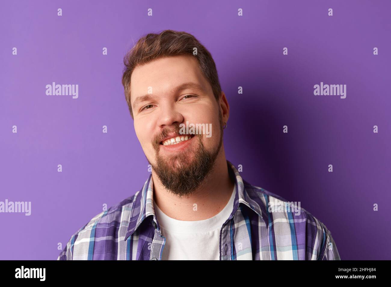 Happy bearded man in shirt smiling looking at camera on purple background. Young handsome stylish guy Stock Photo