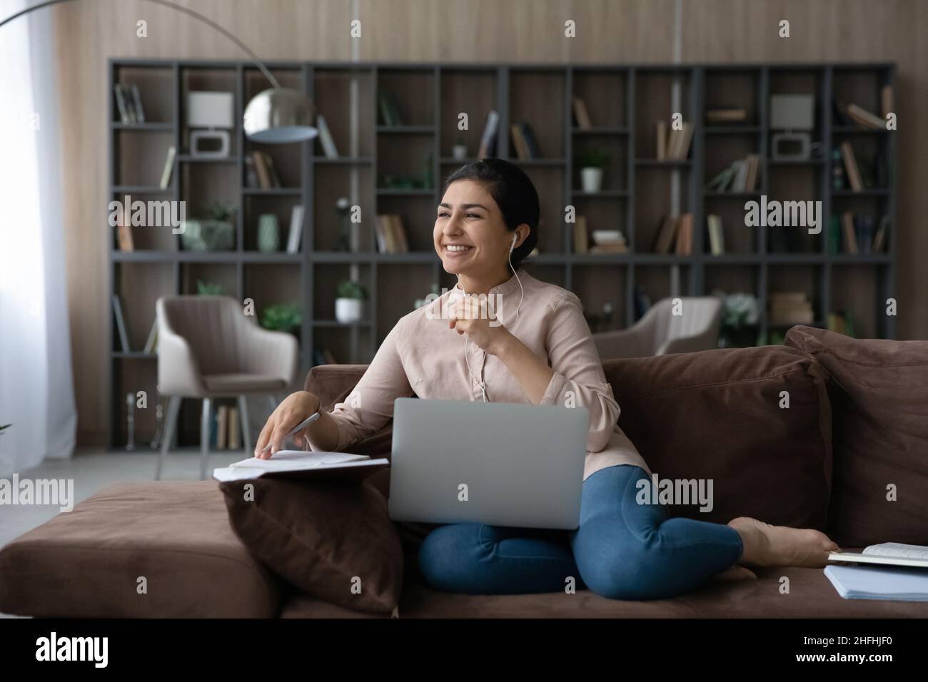 Happy young dreamy Indian woman studying online. Stock Photo
