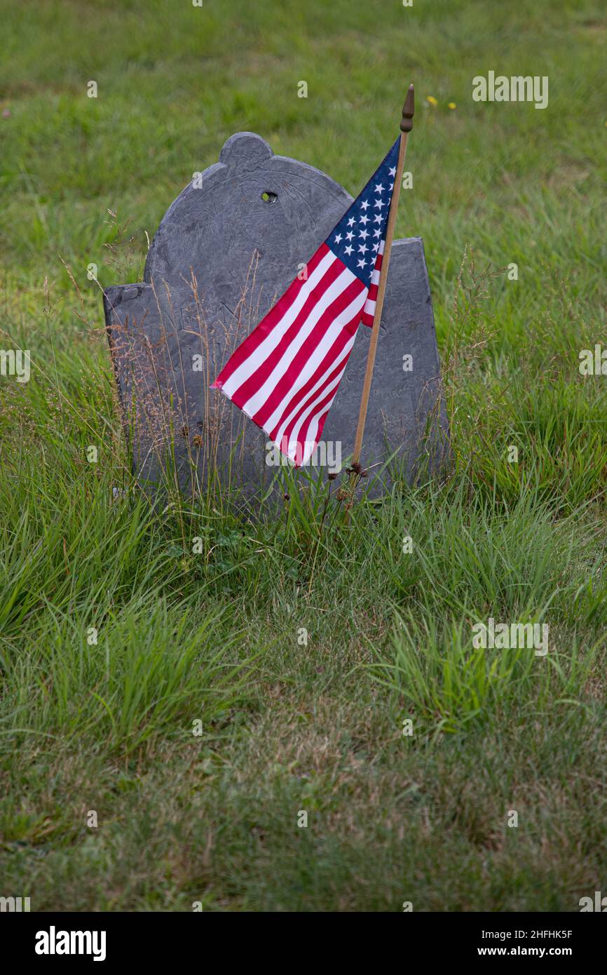 An American flag flies beside a gravestone in Center Cemetery, New Salem, MA Stock Photo