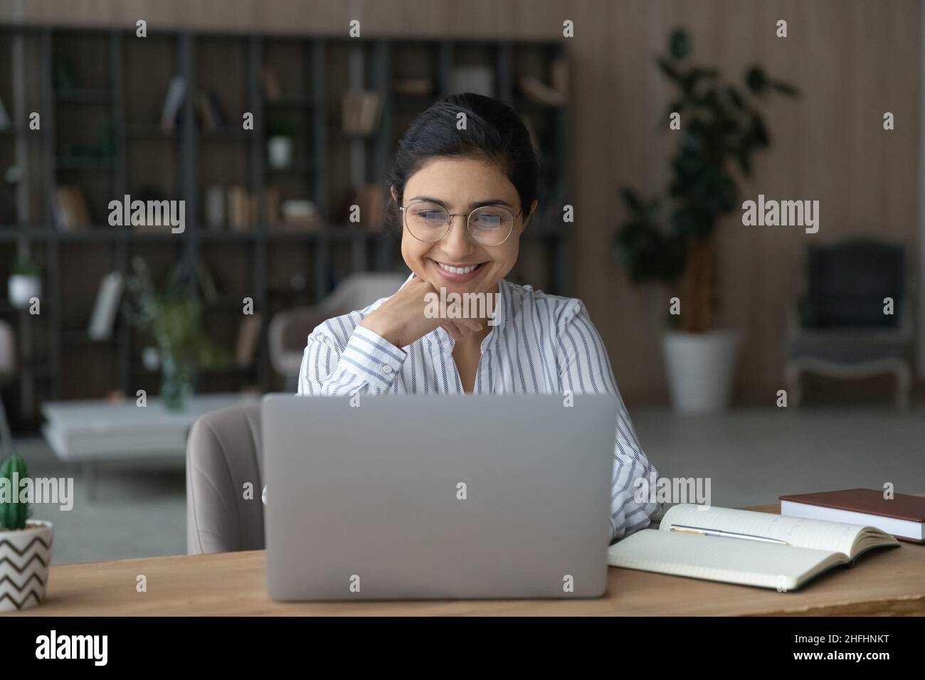 Smiling motivated Indian businesswoman in eyeglasses working on laptop. Stock Photo