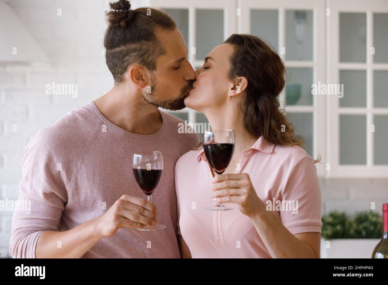 Affectionate loving young family couple kissing, clinking glasses. Stock Photo