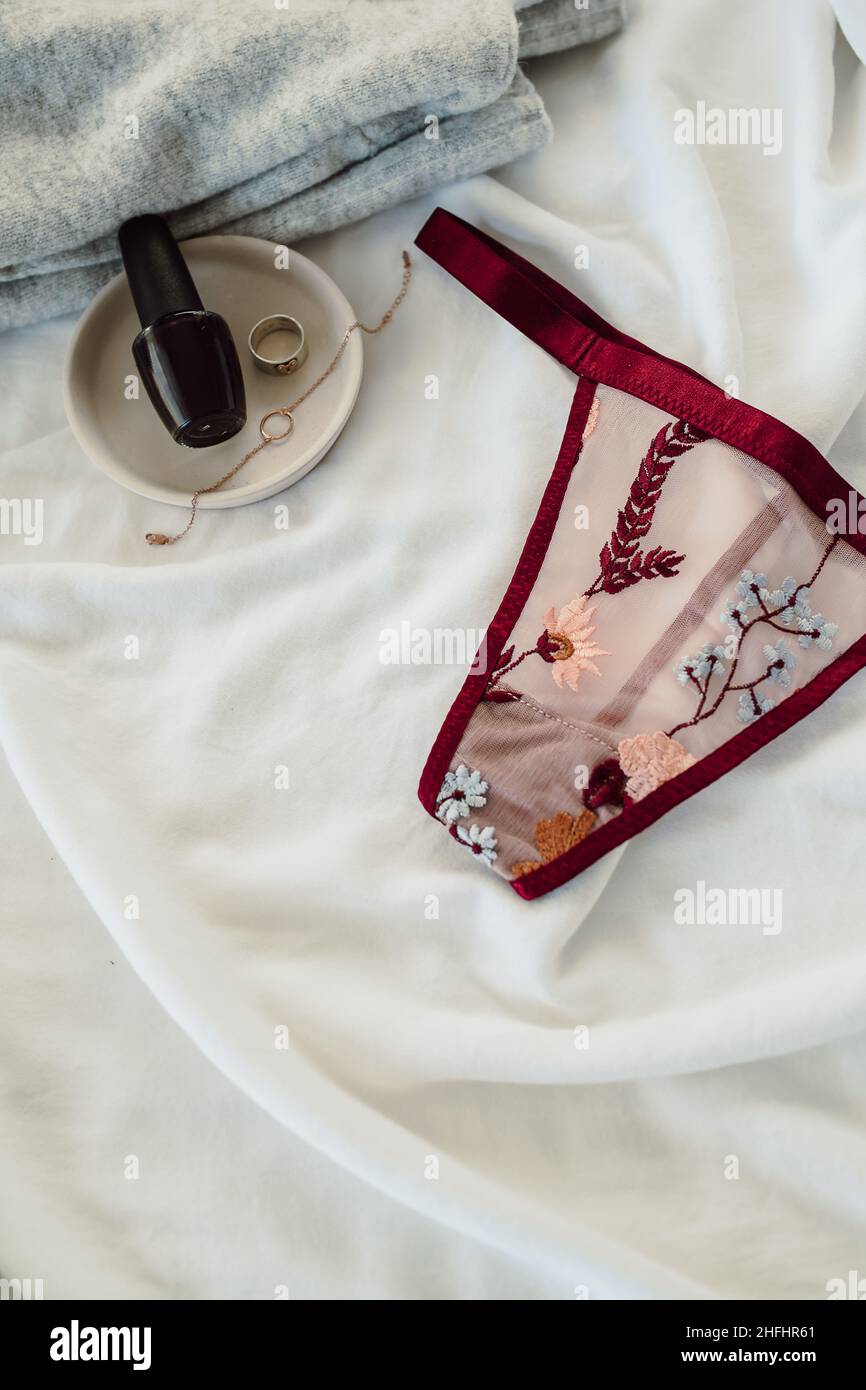Red Sheer Lace Thong with Delicate Floral Embroidery on White Background with Accessories. Valentine Flat Lay. Sexy Underwear for Honeymoon. Stock Photo