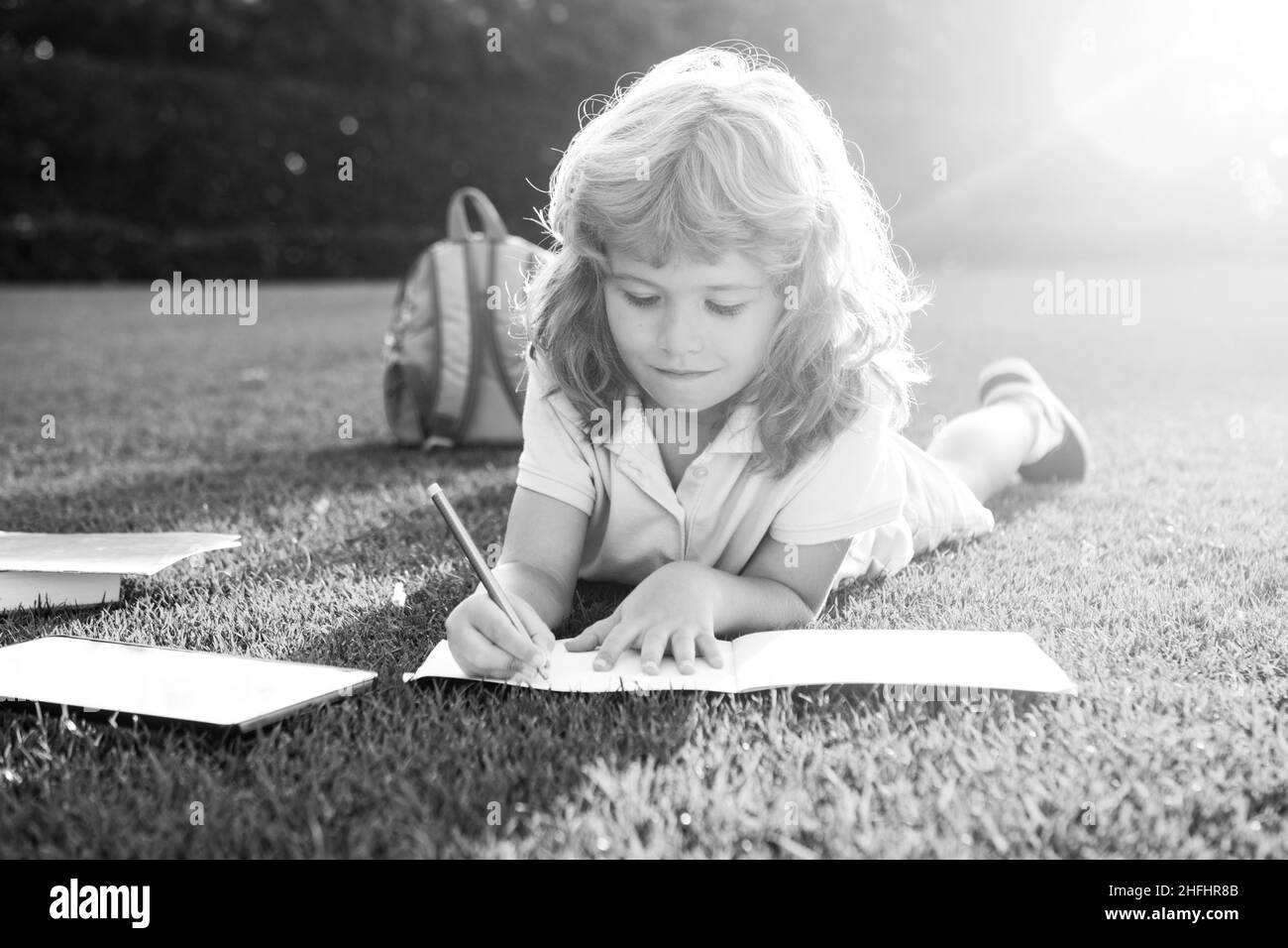 Cute childr boy with books with pencil writing on notebook outdoors