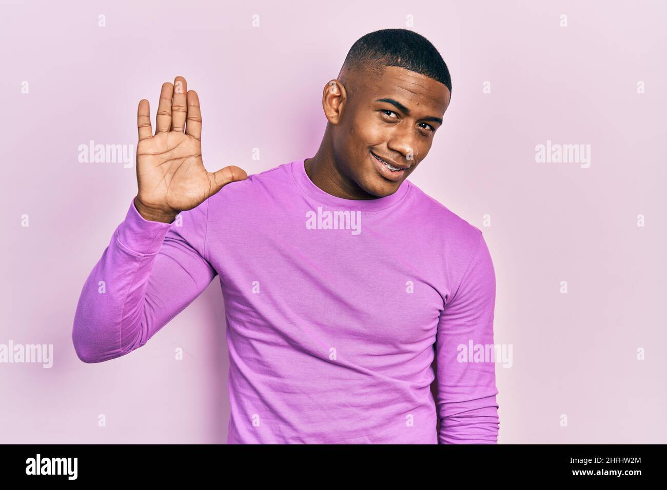 Young black man wearing casual pink sweater waiving saying hello happy ...