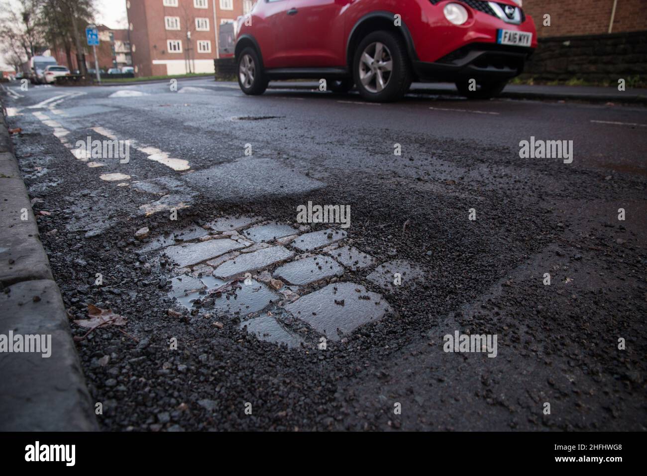 A large pothole exposing brick work in the road Stock Photo