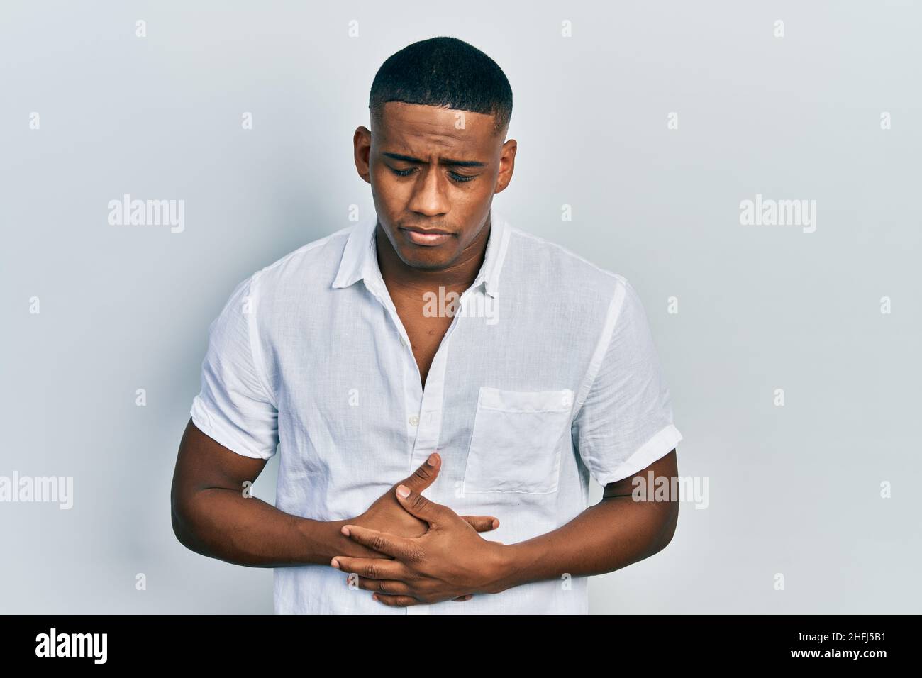 Young black man wearing casual white shirt with hand on stomach because ...