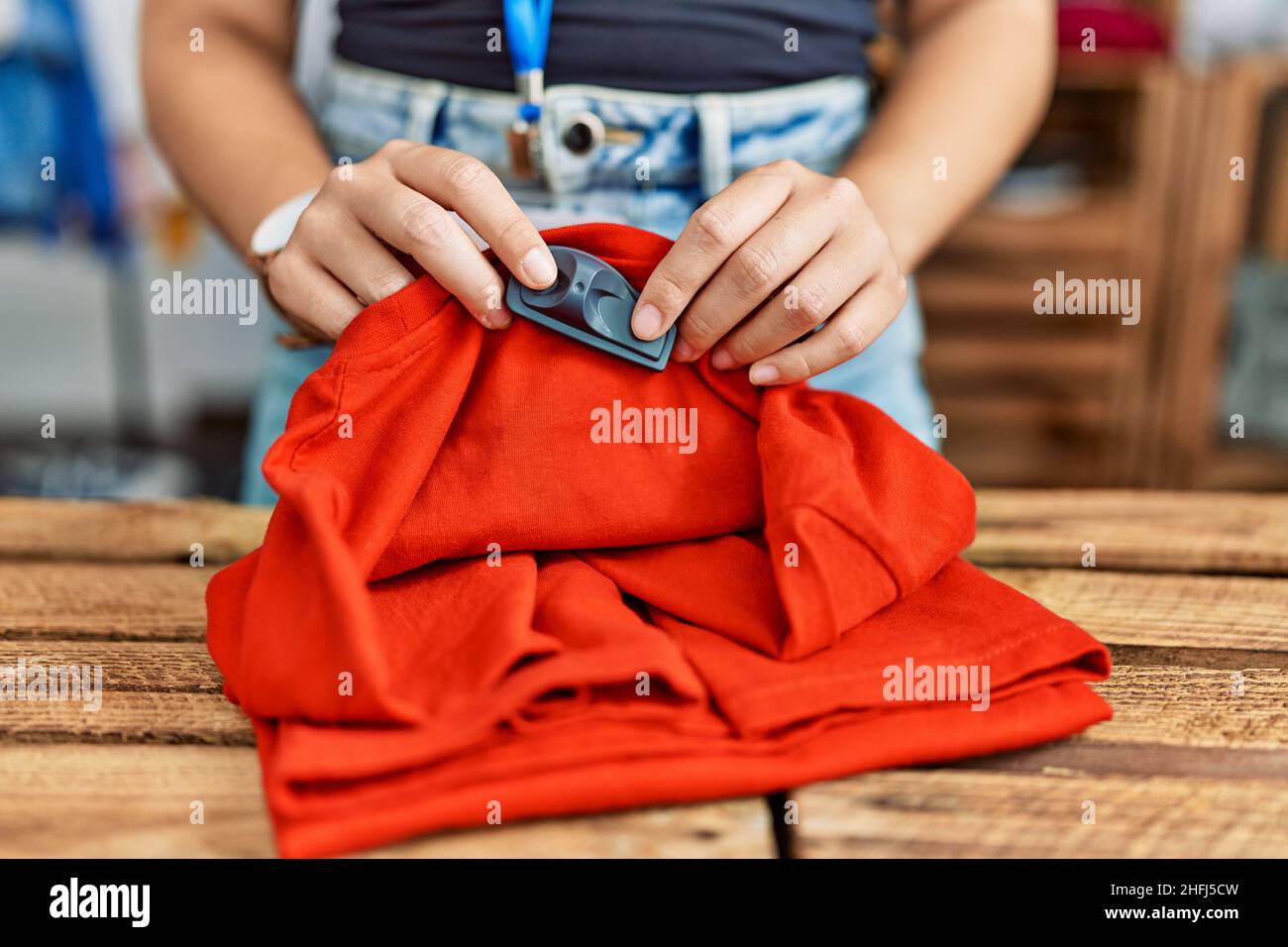 Young hispanic woman touching security alarm clothes at clothing store