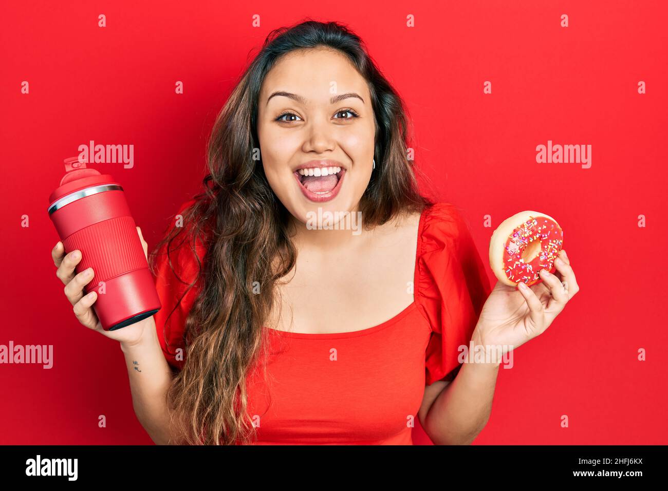 Young hispanic girl eating doughnut and drinking coffee celebrating ...