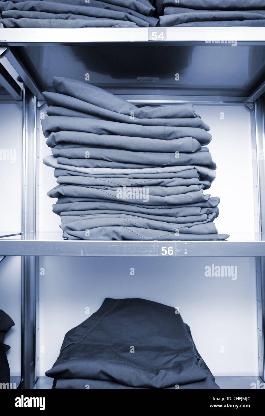 Warehouse shelves with uniform clothes stacked in a pile with size markings. Stock Photo