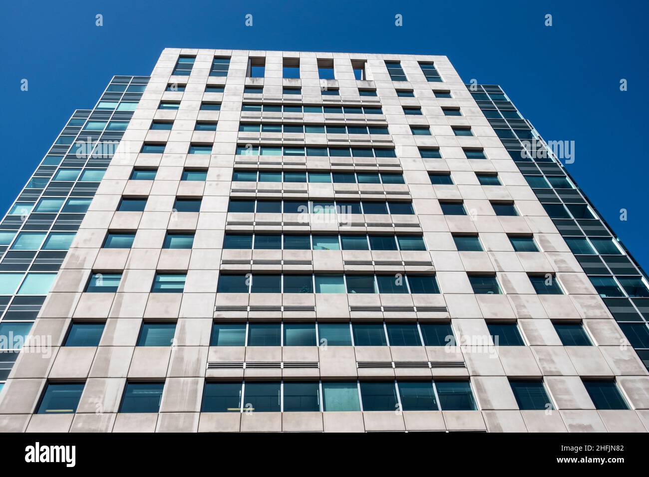 Angled view of a large, window covered apartment building corner against a blue, cloud filled sky Stock Photo