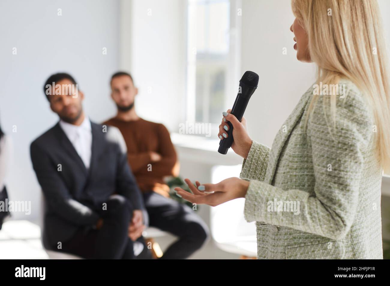 Female business speaker holding a microphone and giving a speech to a diverse audience Stock Photo
