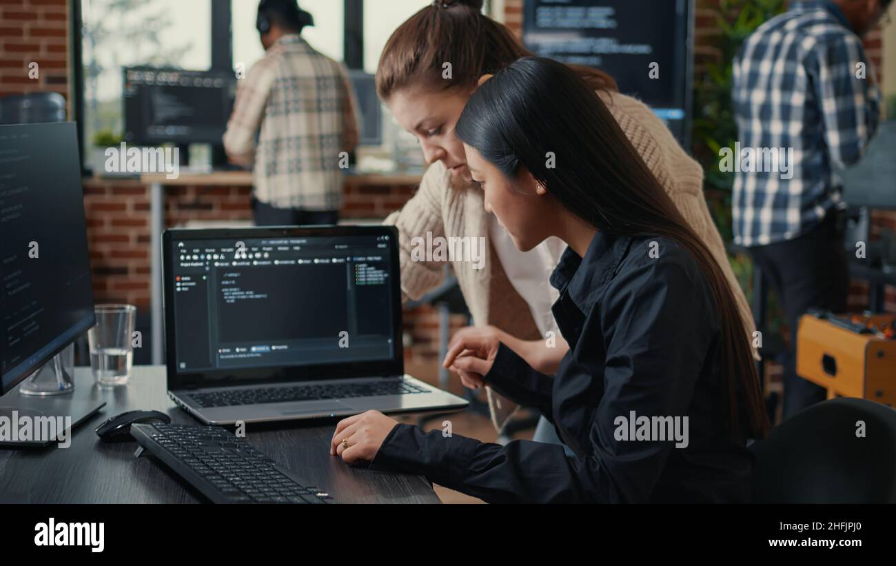 Team of software developers talking about source code running on laptop screen while sitting at desk artificial intelligence server room. Database admins collaborating on data coding group project. Stock Photo