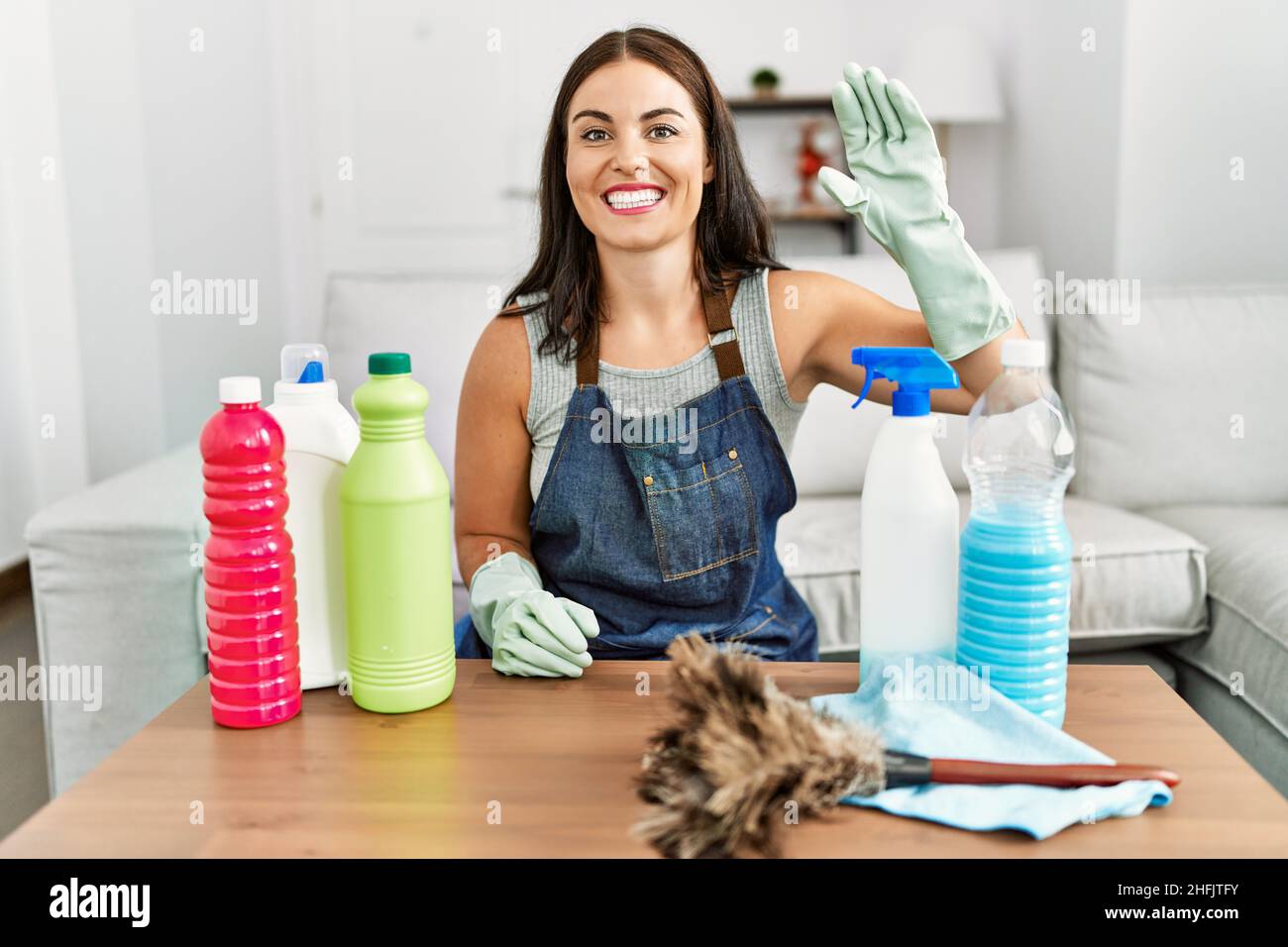 Young brunette woman wearing cleaner apron and gloves cleaning at home ...