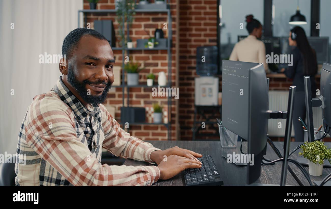 Database programer writing code and smiling while coworker walks by holding clipboard in it agency. Relaxed app developer typing on keyboard with colleagueas computing big data. Stock Photo