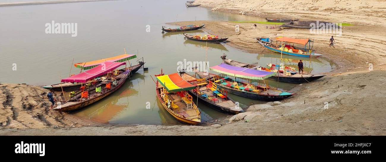 Local wooden boats beached along the banks of the Meghna river, waiting for passengers or tourists, in Rajshahi, a north western division in Bangladesh. The Meghna River is one of the major rivers in Bangladesh, one of the three that form the Ganges Delta the largest delta on earth, which fans out to the Bay of Bengal. The Meghna is formed due to the confluence of the Surma and Kushiyara rivers originating from the hilly regions of eastern India down to Chandpur. Meghna is hydrographically referred to as the Upper Meghna. After the Padma joins, it is referred to as the Lower Meghna. Stock Photo