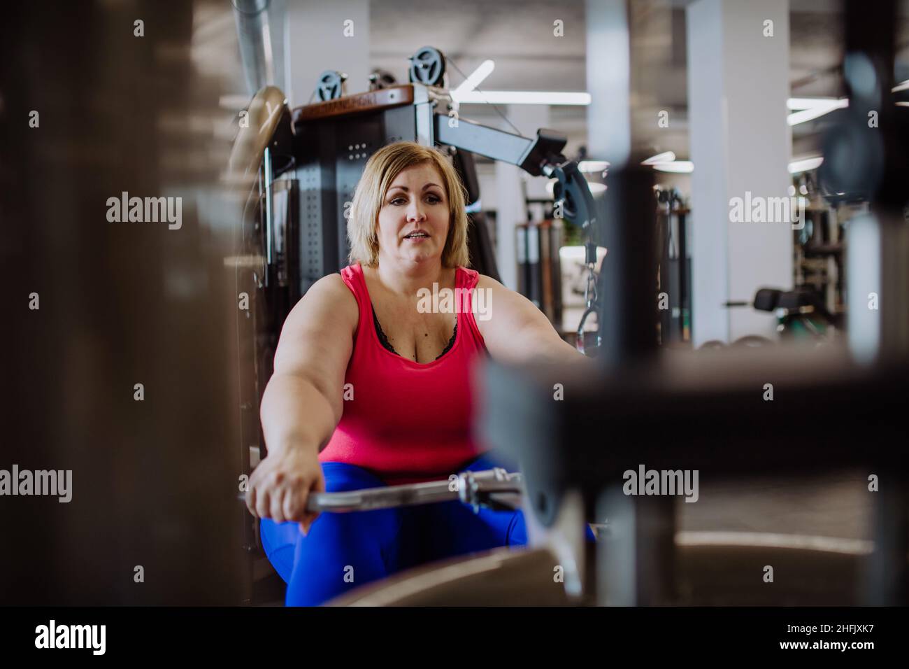 Plus size woman training on rowing machine indoors in gym Stock Photo