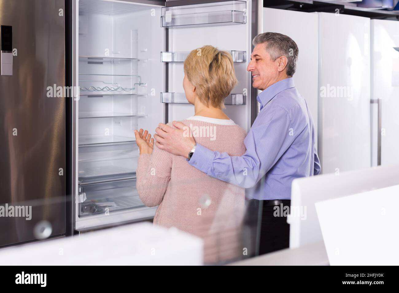 interested mature married couple in shop of household appliances are choosing home modern refrigerator Stock Photo