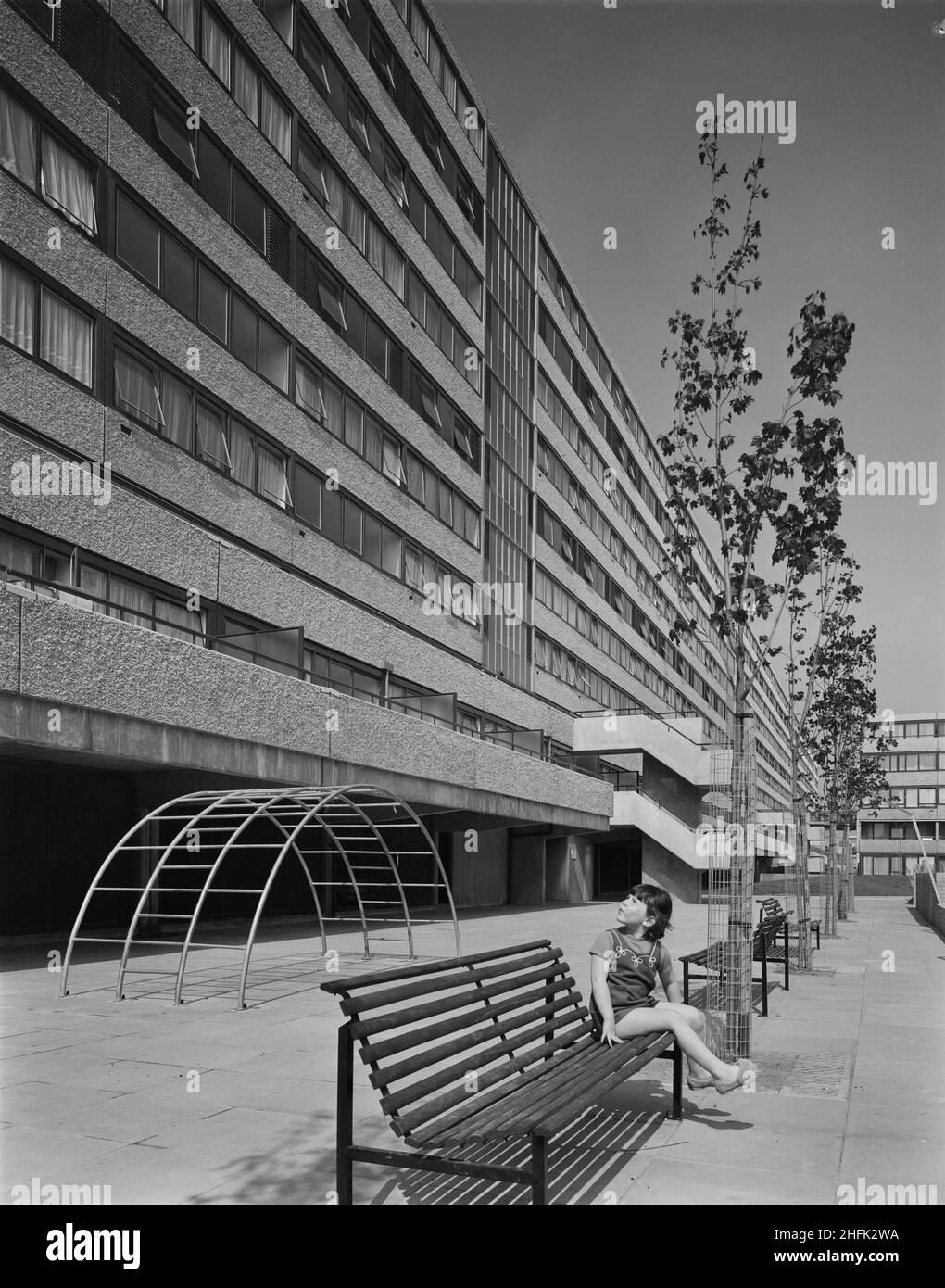 Aylesbury Estate, Walworth, Southwark, London, 01/05/1971. A young girl seated on a bench in front of a recently completed block of flats on the Aylesbury Estate, built using the 12M Jespersen system. In 1963, John Laing and Son Ltd bought the rights to the Danish industrialised building system for flats known as Jespersen (sometimes referred to as Jesperson). The company built factories in Scotland, Hampshire and Lancashire producing Jespersen prefabricated parts and precast concrete panels, allowing the building of housing to be rationalised, saving time and money. Laing's Southern Region st Stock Photo
