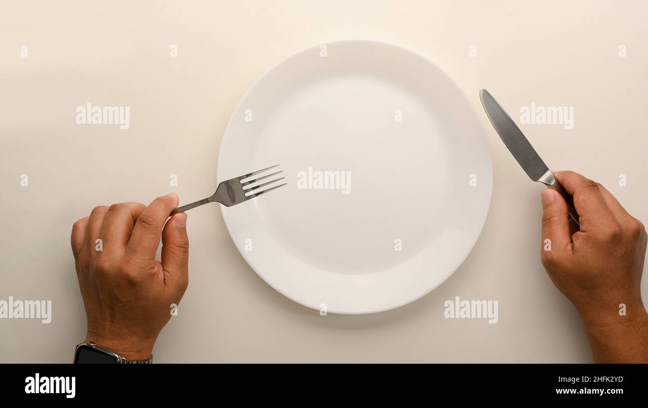 Top view image of a man holding fork and knife over dining table. Blank