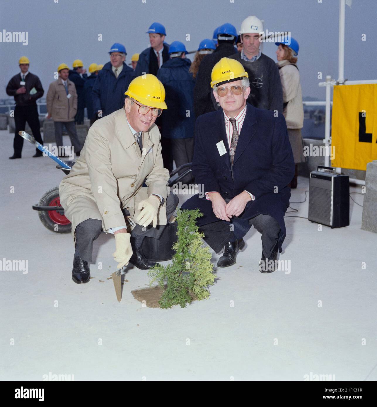 Chelsea and Westminster Hospital, Fulham Road, Kensington and Chelsea, London, 28/01/1991. Sir William Doughty and John Allen crouched beside a coniferous sprig planted in concrete during the topping out ceremony at Chelsea and Westminster Hospital. Laing Management Contracting worked on the construction of Chelsea and Westminster Hospital on behalf of the North West Thames Regional Health Authority between 1989 and 1993. The new teaching hospital was built on the site of the old St Stephen&#x2019;s Hospital, which was demolished in the early months of 1989. The use of fast track construction Stock Photo