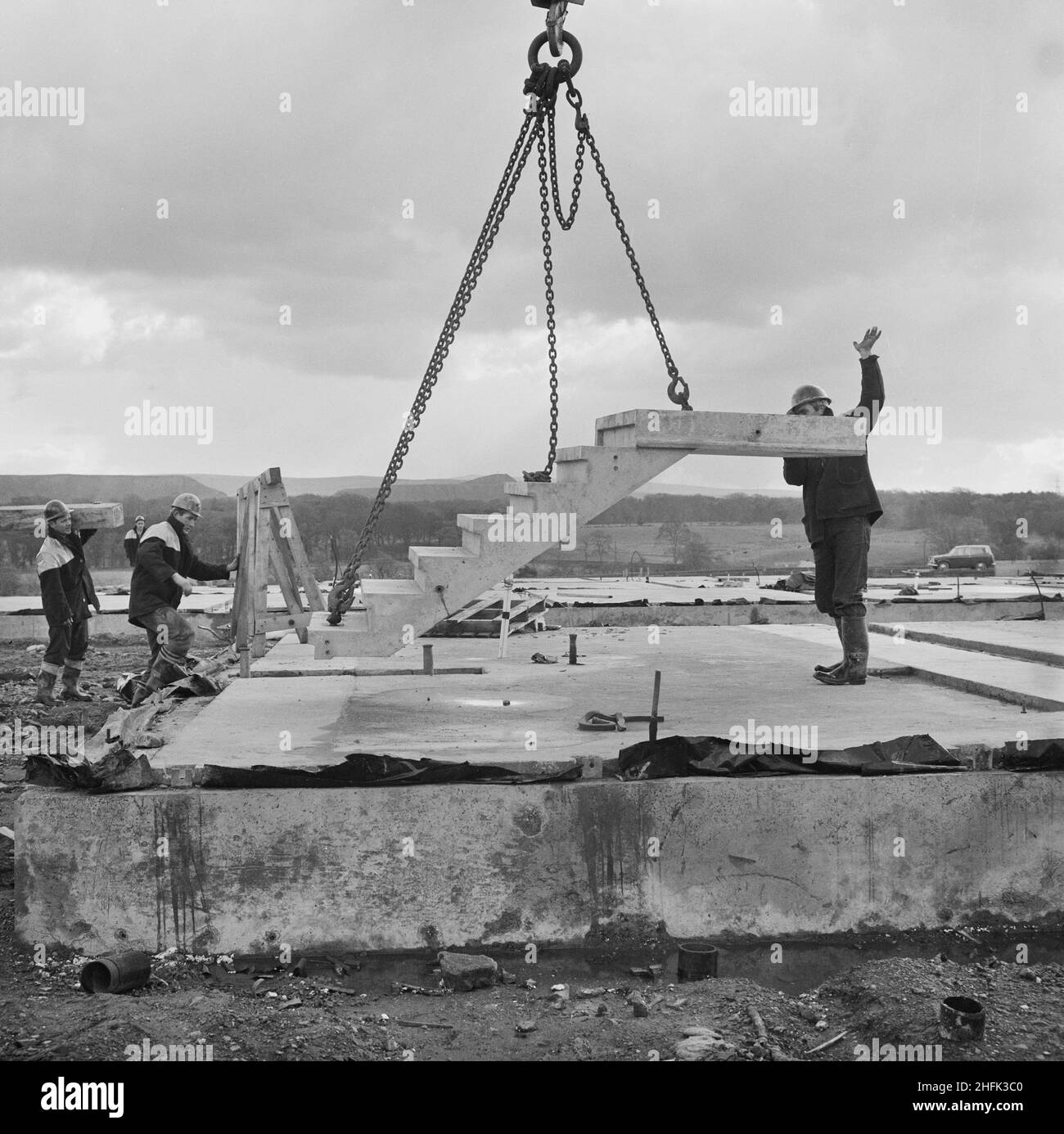 Craigshill, Livingston, West Lothian, Scotland, 01/10/1965. A team of Laing workers lowering a prefabricated concrete staircase into position at a Jespersen construction compound, probably at the Craigshill development in Livingston. In 1963, John Laing and Son Ltd bought the rights to the Danish industrialised building system known as Jespersen (sometimes referred to as Jesperson). The company built factories in Scotland, Hampshire and Lancashire producing Jespersen prefabricated parts and precast concrete panels, allowing the building of housing to be rationalised, saving time and money. The Stock Photo