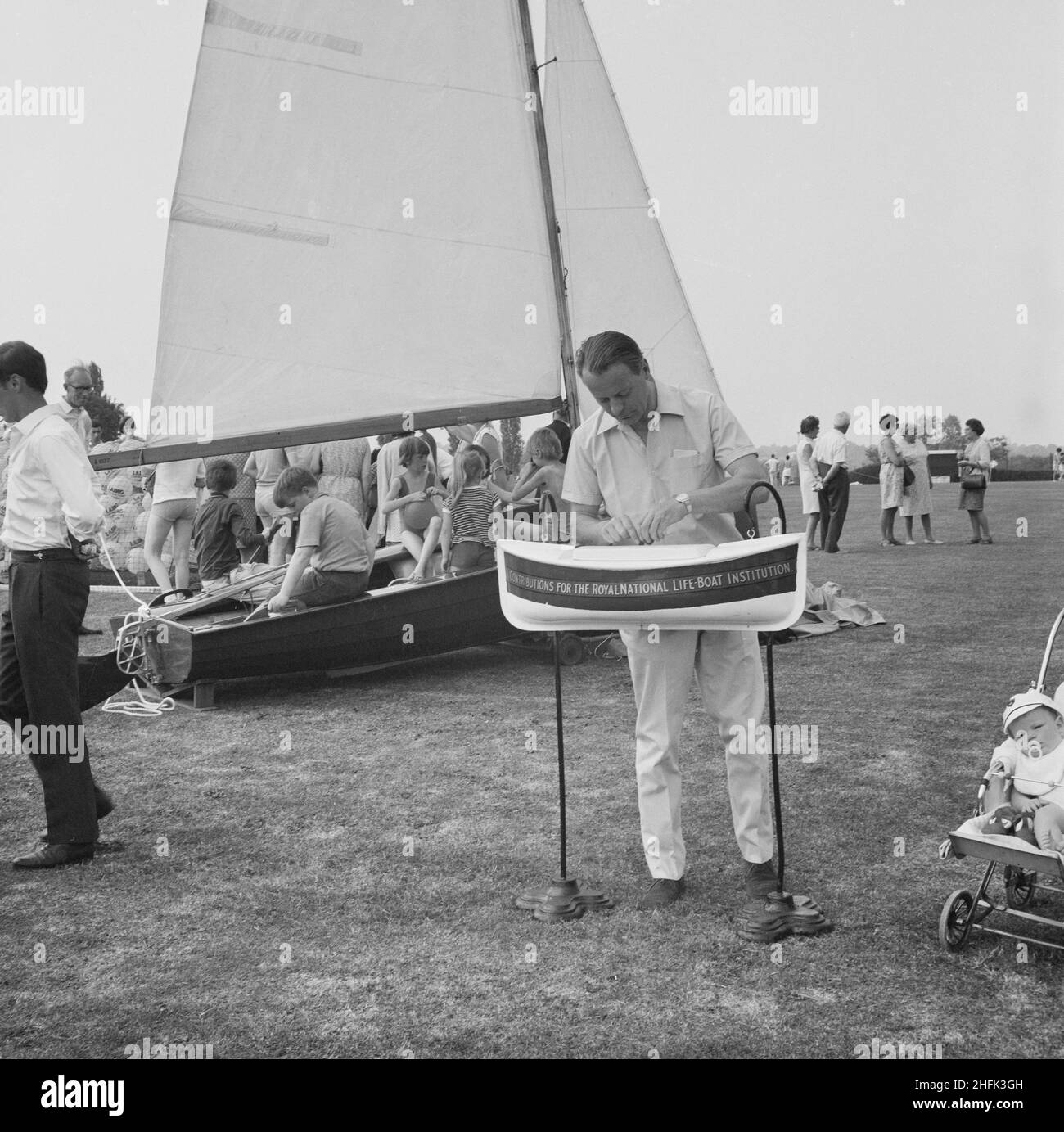 Laing Sports Ground, Rowley Lane, Elstree, Barnet, London, 14/06/1969. A man with a RNLI lifeboat collection box at the Laing Sports Ground, with children in the background sitting in a boat on the grass. A Gala Day was held by Laing at the Laing Sports Ground on 14th June 1969, as a replacement of the annual Sports Day. Sports events were held by the Sports Club, which included hockey, tennis, bowls, and football tournaments. A traditional English fete programme featured coconut shies, bingo, pony rides, catering and a beer tent, candy floss, and roundabouts. The day ended with a beauty conte Stock Photo