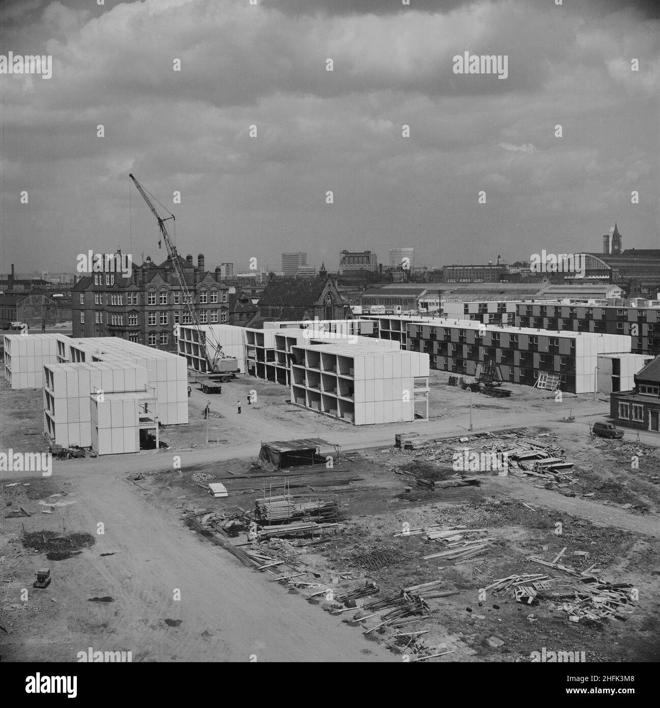 Hulme, Manchester, 04/05/1967. A view over the construction site of three-storey flats in Hulme, built using the 12M Jespersen system, with the Manchester skyline in the distance including Manchester Central Railway Station. In 1963, John Laing and Son Ltd bought the rights to the Danish industrialised building system known as Jespersen (sometimes referred to as Jesperson). The company built factories in Scotland, Hampshire and Lancashire producing Jespersen prefabricated parts and precast concrete panels, allowing the building of housing to be rationalised, saving time and money. These flats Stock Photo