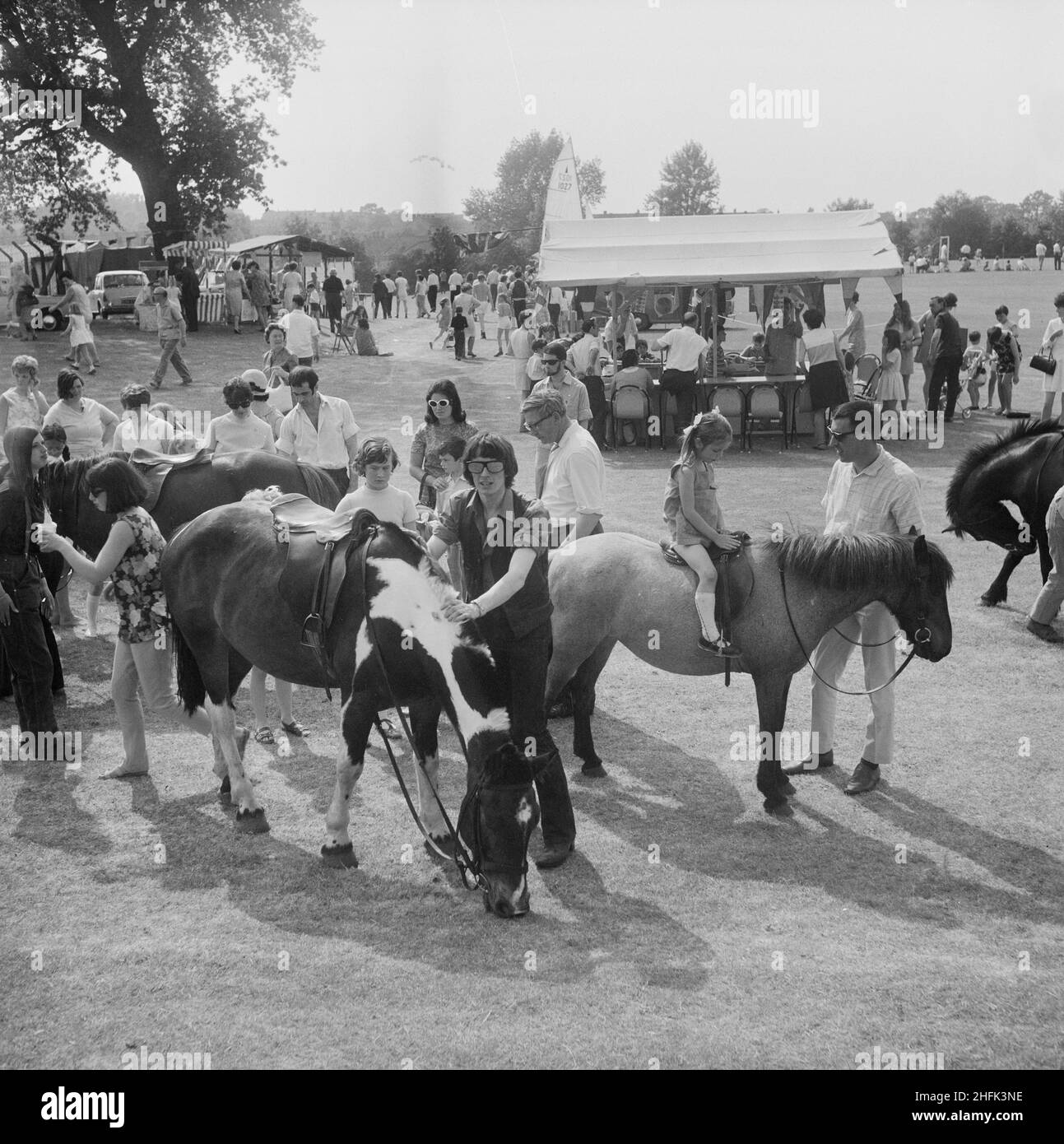 Laing Sports Ground, Rowley Lane, Elstree, Barnet, London, 14/06/1969. A Gala Day at the Laing Sports Ground at Elstree, showing children's pony rides in the foreground with stalls and crowds beyond. A Gala Day was held by Laing at the Laing Sports Ground on 14th June 1969, as a replacement of the annual Sports Day. Sports events were held by the Sports Club, which included hockey, tennis, bowls, and football tournaments. A traditional English fete programme featured coconut shies, bingo, pony rides, catering and a beer tent, candy floss, and roundabouts. The day ended with a beauty contest, p Stock Photo