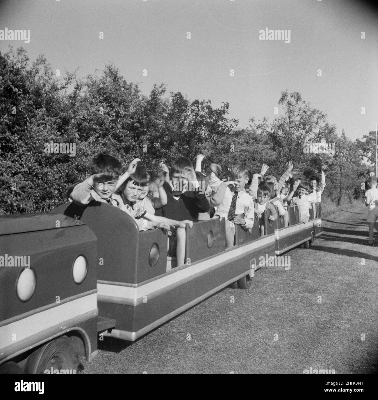 Laing Sports Ground, Rowley Lane, Elstree, Barnet, London, 18/06/1955. Children riding in a miniature train carriage and waving at the camera during a Laing sports day at Elstree. This sports day was attended by people from Laing contracts in Thurleigh, Bradford, Harlow, Shell Haven, London, Welwyn Garden City, Leicester and even as far as Plymouth. The day included field and track competitions as well as special attractions including Scottish dancing, a flower show, gymnastic displays and music by the Silver Band of the 5th Hendon Company Boys' Brigade. Stock Photo