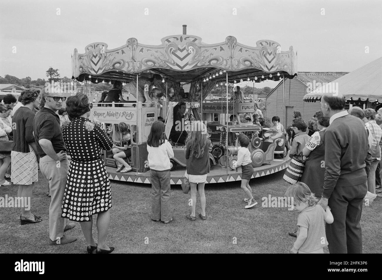 Laing Sports Ground, Rowley Lane, Elstree, Barnet, London, 09/06/1973. People standing around a children's carousel at the annual Gala Day held at the Laing Sports Ground at Elstree. The annual Gala Day was held at the Laing Sports Ground on 9th June 1973. Attractions included police dog demonstrations, model aircraft, the Royal British Legion band, children's races, and sports. In the evening there was dancing and bingo in the Club House, and 'beer and beat' in the marquee. Over 2,000 people attended the gala, and over 600 people stayed for the evening entertainment. Stock Photo