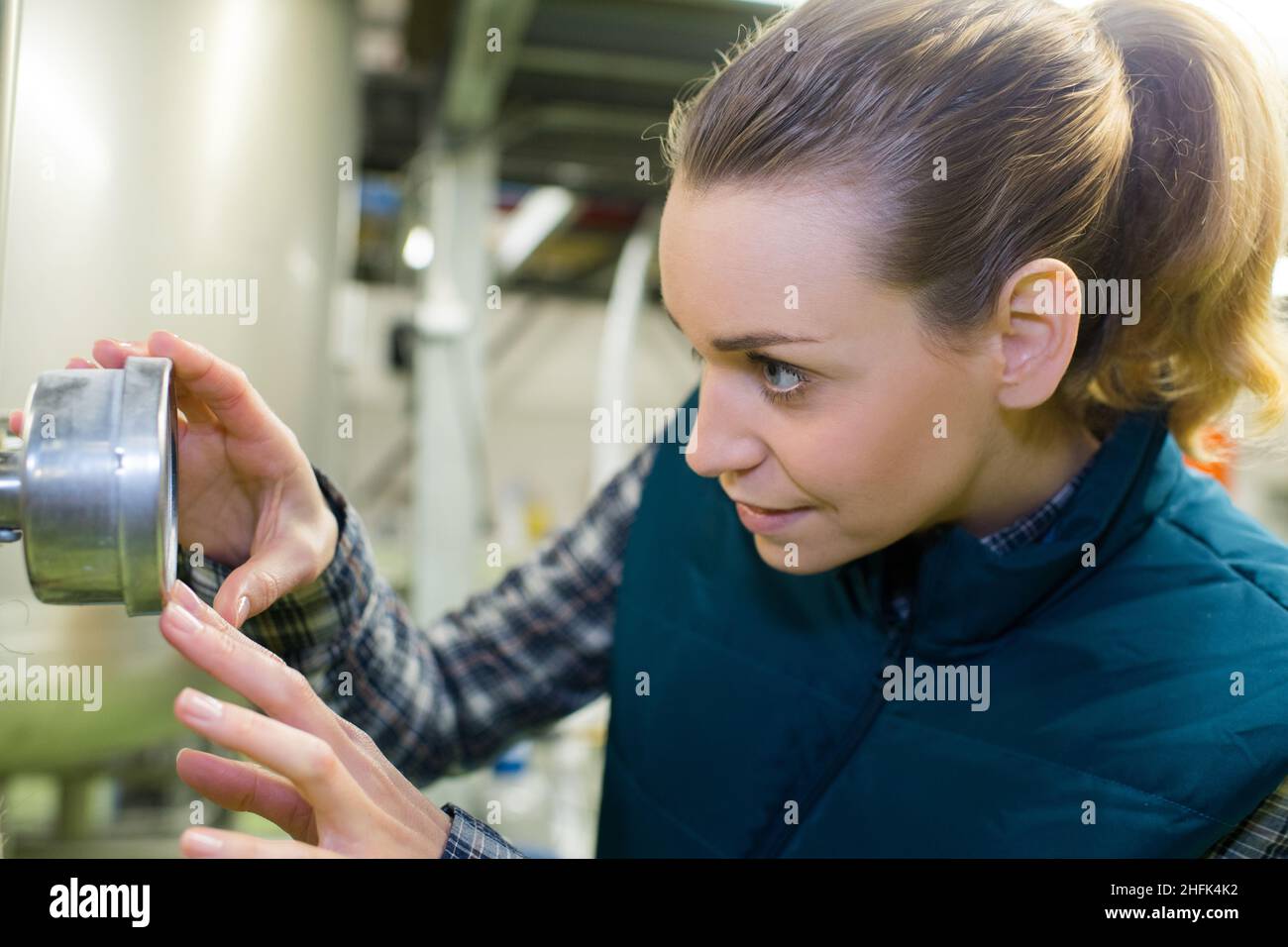 efficient female engineer rotating valve on tank inside factory Stock Photo