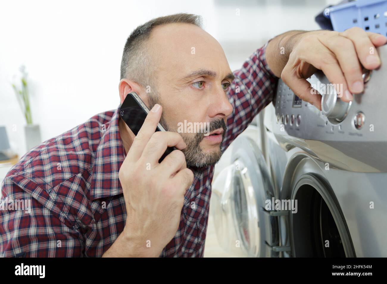 man using smart phone while doing laundry Stock Photo