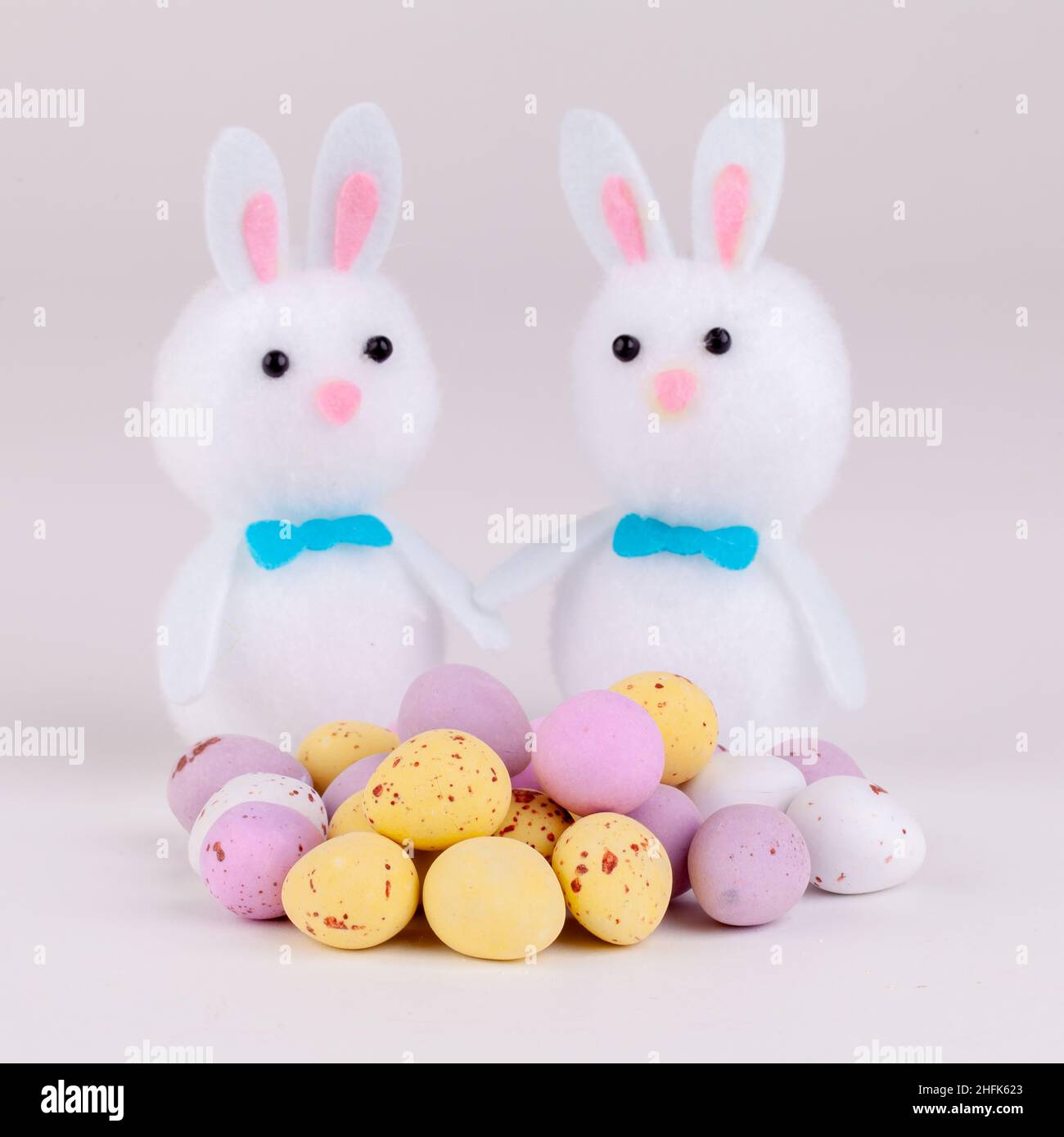 Easter bunnies with candy covered chocolate easter eggs on a plain grey background Stock Photo
