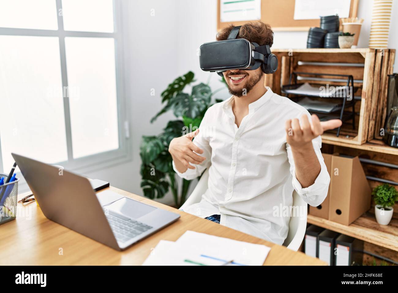 Young arab man using vr goggles doing guitar gesture at office Stock Photo